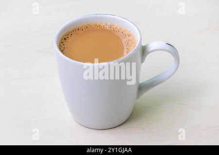 Una tazza di tè al latte caldo o di dudh cha in una tazza di ceramica bianca su una superficie di legno chiaro. Foto Stock