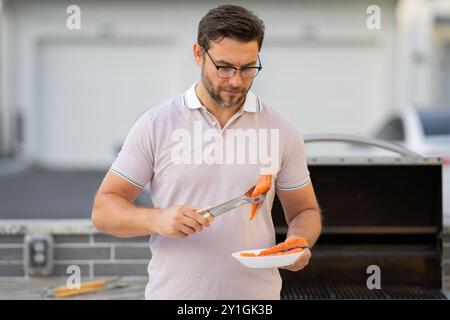 Uomo a un barbecue. Cuoco maschile che prepara barbecue di filetto di salmone all'aperto. Carne al barbecue, grigliate per picnic. Manzo arrosto. Cuocere la preparazione del barbecue nel Foto Stock