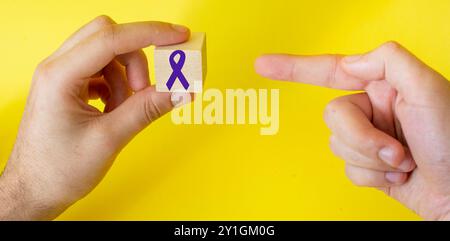 Il nastro viola su un cubo mostra un dito su uno sfondo giallo. A sostegno della giornata mondiale del cancro e della campagna per la giornata dell'Alzheimer. Foto Stock