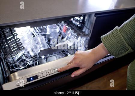 La mano della donna si accende in lavastoviglie per lavare i piatti. Elettrodomestici incorporati in cucina Foto Stock