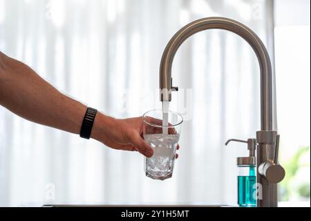 Persona che riempie un bicchiere d'acqua. Messa a fuoco selettiva su vetro, ripresa verticale. Foto Stock
