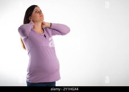Dolore al collo in una ragazza incinta in una camicetta viola su sfondo bianco. Il concetto di osteocondrosi e protrusione della colonna cervicale, esacerbati Foto Stock