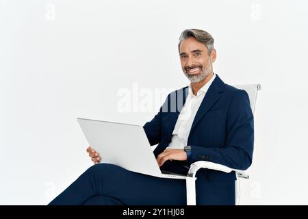 Uomo d'affari maturo e felice che utilizza un computer portatile seduto su una sedia isolata su una parete bianca. Foto Stock