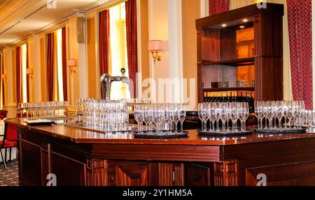 Un'area bar splendidamente arredata presenta numerosi bicchieri scintillanti su un bancone in legno lucido, con un decor elegante e una luce soffusa sullo sfondo Foto Stock