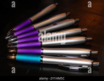 Una collezione di penne colorate disposte in fila, con colori viola, argento e tè. Le penne hanno un design elegante e sono posizionate su una tavola scura Foto Stock