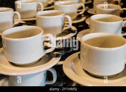 Una vista ravvicinata di più tazze di caffè bianche disposte su piattini, che mostrano il loro design semplice ed elegante. Le tazze sono impilate in modo ordinato, creando un Foto Stock