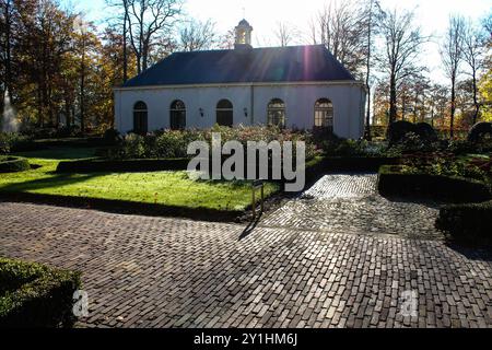 Un tranquillo giardino caratterizzato da un affascinante edificio bianco circondato da vegetazione lussureggiante e fiori colorati. La luce del sole filtra attraverso gli alberi, create Foto Stock