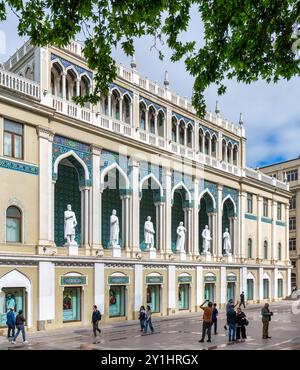 Baku, Azerbaigian - 5 maggio 2024: Museo Nizami dell'Azerbaigian, con statue che fiancheggiano la facciata. L'edificio e' decorato con archi e intricati lavori di piastrelle. Le persone possono essere viste camminare vicino all'edificio Foto Stock
