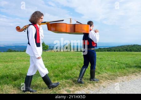 Due uomini in costumi popolari che trasportano strumenti musicali Contrabass Strání Repubblica Ceca Europa Foto Stock