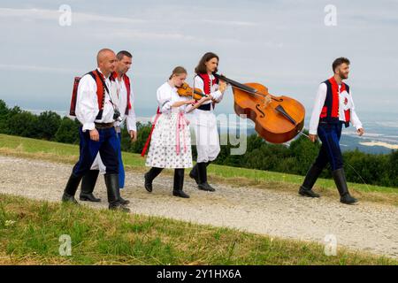 Gruppo di musicisti in costumi popolari tradizionali che camminano lungo un sentiero rurale, uno che suona un violino e l'altro che porta un contrabbasso Foto Stock