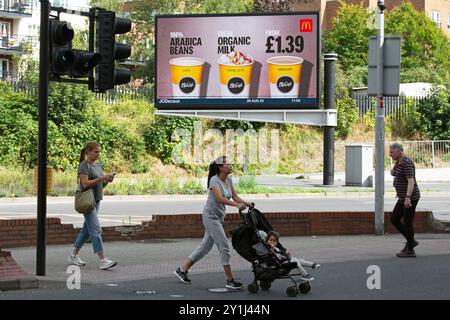 tre persone attraversano una strada a kingston, surrey, inghilterra, di fronte a un cartellone digitale che pubblicizza tre tipi di caffè offerti dal mcdonalds mccafe Foto Stock