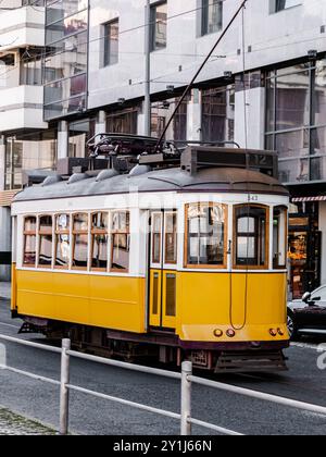 Un tram d'epoca giallo luminoso che si muove per le strade di Lisbona, combinando il fascino del vecchio mondo con un ambiente moderno Foto Stock