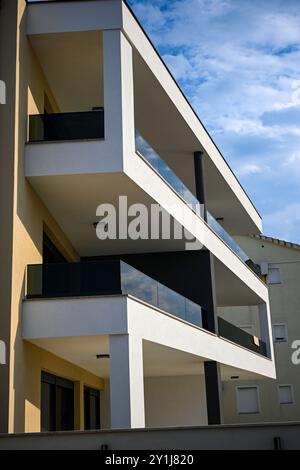 Forme geometriche di un moderno edificio bianco che mostra balconi con ringhiera di vetro sotto il cielo blu. Foto Stock