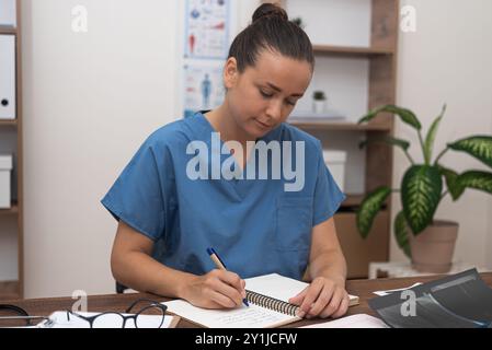 Il medico di sesso femminile in uniforme medica blu lavora con la documentazione medica seduta in ufficio Foto Stock