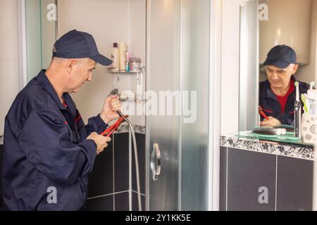 L'idraulico maturo cambia il rubinetto della doccia utilizzando pinze per utensili, foto ravvicinata. Impianto idraulico, riparazione, assemblaggio. Foto Stock