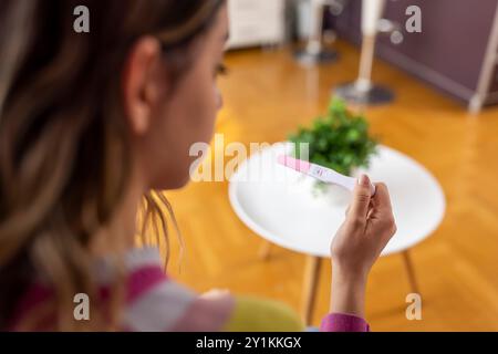 Teenager ragazza spaventata e scioccata tenendo il test di gravidanza risultato positivo che sembra infelice e in depressione. Concetto inaspettato di ragazza incinta Foto Stock