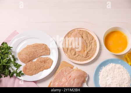 Fare schnitzel. Fette di carne con briciole di pane e ingredienti su un tavolo di legno bianco, distesa piatta Foto Stock