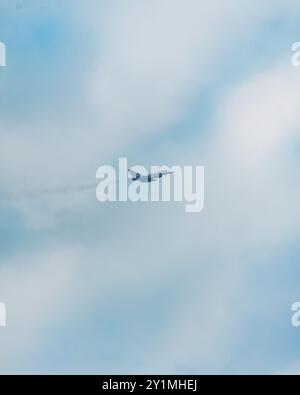 Vista aerea di un jet da caccia che vola in alto sopra le splendide nuvole, lasciando una coda in un cielo azzurro. Foto Stock