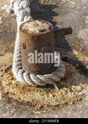 Vecchia nave ormeggiata con attrezzature intemperie, nodo legato e tacca metallica sul molo commerciale Foto Stock