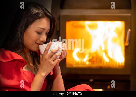 Una donna con un vestito rosso beve dalla grande tazza davanti al fornello Foto Stock