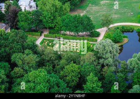 Vista aerea di un giardino splendidamente paesaggistico con motivi intricati, circondato da lussureggianti alberi verdi e da un tranquillo laghetto. Le persone si possono vedere divertendosi Foto Stock