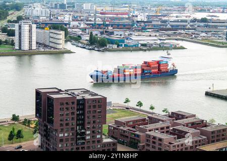 Vista aerea di un porto affollato con una grande nave portacontainer che naviga lungo il fiume. Gli edifici circostanti e le aree industriali sono visibili, mettendo in risalto le aree urbane Foto Stock