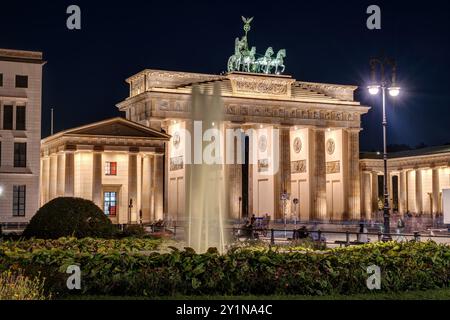 La porta di Brandeburgo illuminata di Berlino con una fontana di notte Foto Stock