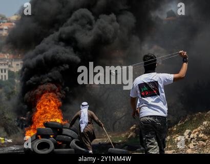 Qalqilia, Palestina. 5 luglio 2019. I manifestanti palestinesi si scontrano con i soldati israeliani nella città della Cisgiordania di Kafr Qaddum durante la loro protesta settimanale del venerdì contro gli insediamenti israeliani illegali. Alcuni palestinesi hanno bruciato pneumatici e lanciato pietre contro le forze israeliane che hanno sparato gas lacrimogeni e proiettili rivestiti di gomma ai manifestanti ferendone almeno quattro. Dal luglio 2011, i residenti di Kafr Qaddum e dei villaggi limitrofi organizzano proteste il venerdì contro l’estensione del vicino insediamento israeliano di Qadumim, la chiusura ai palestinesi della strada principale del villaggio e il Foto Stock