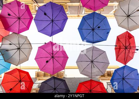 Ombrelli vibranti appesi sulla strada di Catania, Sicilia. Colorata installazione di arte urbana che fornisce ombra e interesse visivo. Prospettiva unica da Foto Stock