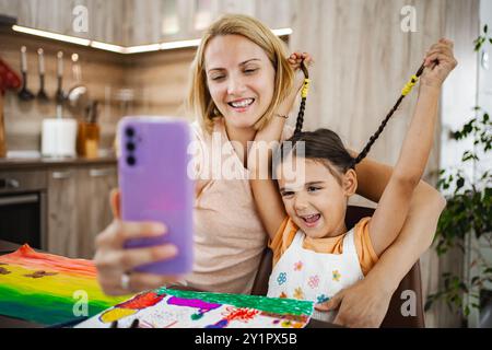 La madre condivide un momento di gioia con sua figlia mentre si fa un selfie a casa Foto Stock