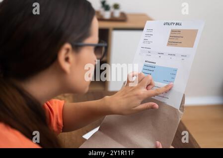 busta in mano, una donna ispeziona attentamente le bollette, esponendo in modo vividamente tasse e costi domestici Foto Stock