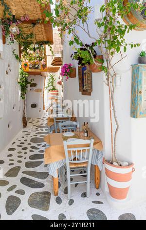 Tavoli e sedie della taverna fiancheggiano una strada bianca nella vecchia zona di Bourgos, nella città di Naxos, nell'isola di Naxos, nelle Cicladi, in Grecia Foto Stock