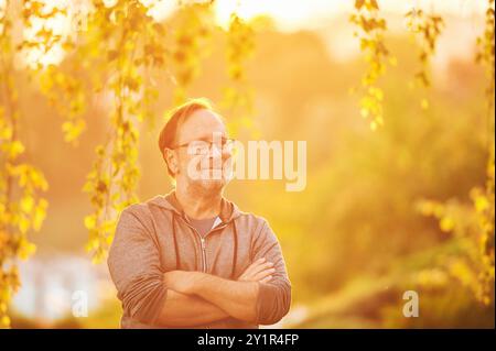 Ritratto all'aperto di un uomo di 50 - 55 anni che si gode di una bella mattina o di una sera con i raggi di luce Foto Stock