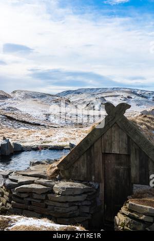 Uomo di mezza età che si gode di sorgenti termali in una piscina naturale in Islanda in inverno con una cabina di legno Foto Stock