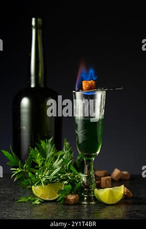 Bruciare lo zucchero su un bicchiere con assenzio. Preparazione della bevanda. Absinthe con ingredienti su sfondo nero. Foto Stock