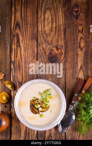 Sul tavolo di legno si trova una zuppa di panna con funghi freschi come base, circondata da verdure fresche. Foto Stock