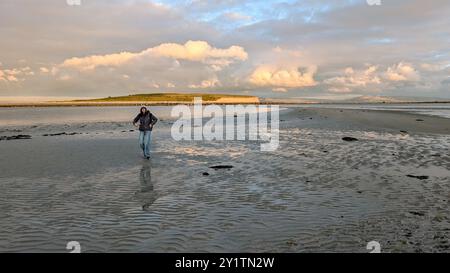 Donna escursionista con zaino in spalla che gode del paesaggio costiero del tramonto sulla spiaggia sabbiosa di Silverstrand, Galway, Irlanda, avventura e stile di vita, persone nella natura Foto Stock