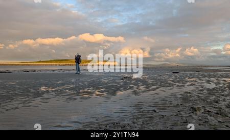 Donna escursionista con zaino in spalla che gode del paesaggio costiero del tramonto sulla spiaggia sabbiosa di Silverstrand, Galway, Irlanda, avventura e stile di vita, persone nella natura Foto Stock