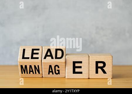 Simbolo Manager vs. Linea di associazione. Un uomo d'affari ha disposto dei cubi di legno sul tavolo per formare le parole "manager" a "leader". Concetto di business. Bellissimo sfondo grigio Foto Stock