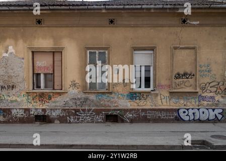 Lato di un vecchio edificio con finestre con persiane che mostrano l'età e i danni insieme a graffiti. Foto Stock