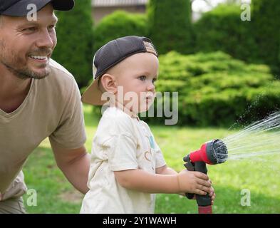 Padre e suo figlio innaffiano il prato con il tubo nel cortile Foto Stock