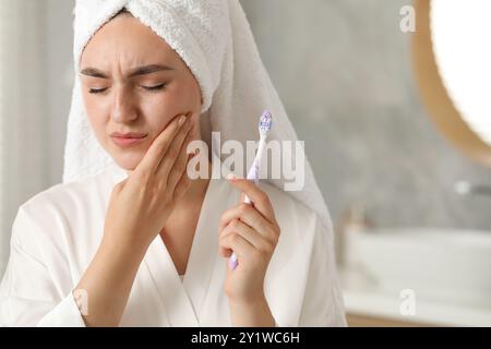 Giovane donna con spazzolino che soffre di mal di denti in bagno Foto Stock