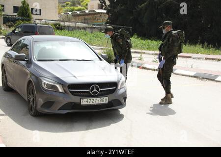 Jenin, West Bank. 23 marzo 2020. I membri delle forze di sicurezza nazionali palestinesi hanno istituito una barriera e svolgono controlli all'ingresso della città di Jenin per far rispettare l'attuazione di nuove misure restrittive contro la diffusione del coronavirus in Cisgiordania. Domenica il primo ministro palestinese ha ordinato un divieto di due settimane su tutti i movimenti non essenziali per contenere la diffusione del COVID-19, mentre il numero di casi confermati in Cisgiordania è salito a 57 Foto Stock