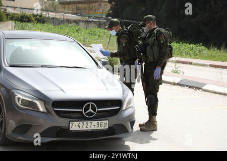 Jenin, West Bank. 23 marzo 2020. I membri delle forze di sicurezza nazionali palestinesi hanno istituito una barriera e svolgono controlli all'ingresso della città di Jenin per far rispettare l'attuazione di nuove misure restrittive contro la diffusione del coronavirus in Cisgiordania. Domenica il primo ministro palestinese ha ordinato un divieto di due settimane su tutti i movimenti non essenziali per contenere la diffusione del COVID-19, mentre il numero di casi confermati in Cisgiordania è salito a 57 Foto Stock