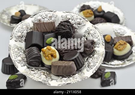 Diversi tipi di praline di cioccolato su piatti d'argento, primo piano, isolate su sfondo bianco Foto Stock
