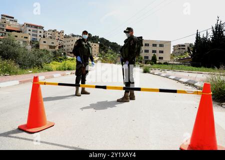 Jenin, West Bank. 23 marzo 2020. I membri delle forze di sicurezza nazionali palestinesi hanno istituito una barriera e svolgono controlli all'ingresso della città di Jenin per far rispettare l'attuazione di nuove misure restrittive contro la diffusione del coronavirus in Cisgiordania. Domenica il primo ministro palestinese ha ordinato un divieto di due settimane su tutti i movimenti non essenziali per contenere la diffusione del COVID-19, mentre il numero di casi confermati in Cisgiordania è salito a 57 Foto Stock