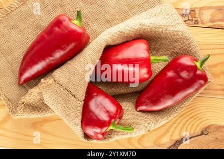 Diversi peperoni rossi dolci con sacchetto di iuta su un tavolo di legno, vista dall'alto. Foto Stock