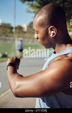 Giovane atleta, giocatore di calcio siede, riposa all'aperto in un campo sportivo, indossa una camicia senza maniche, controlla il suo smartwatch o il fitness tracker, il monitor Foto Stock
