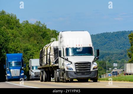 Immagine orizzontale di un autocarro semi-piano che trasporta macchinari pesanti, con un conseguente traffico estivo interstatale. Foto Stock