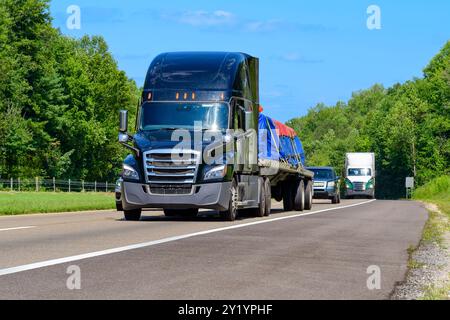 Immagine orizzontale di una diciotto ruote a superficie piana nera che trasporta un carico di macchinari pesanti. Foto Stock